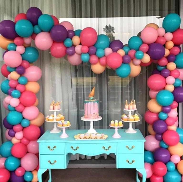 Arco desconstruído com mesa de aniversário na frente, bolos, cupcakes e outros doces